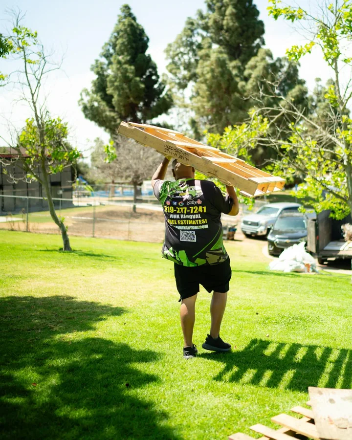 Haul Away Any Day crew member carrying wooden pallets across a yard
